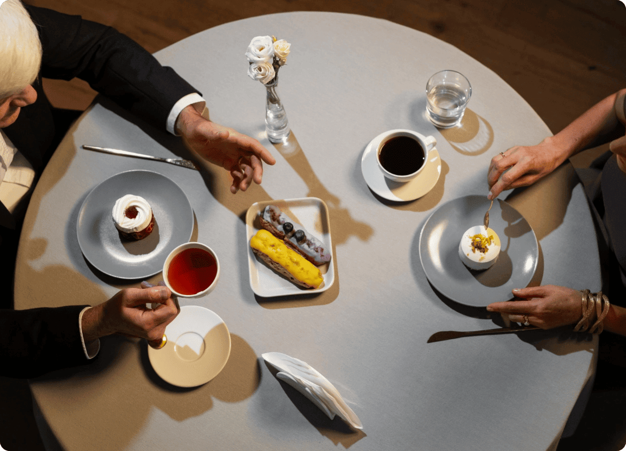 Vue de dessus d'une table où deux personnes partagent un café, un thé et des pâtisseries fines dans une ambiance élégante