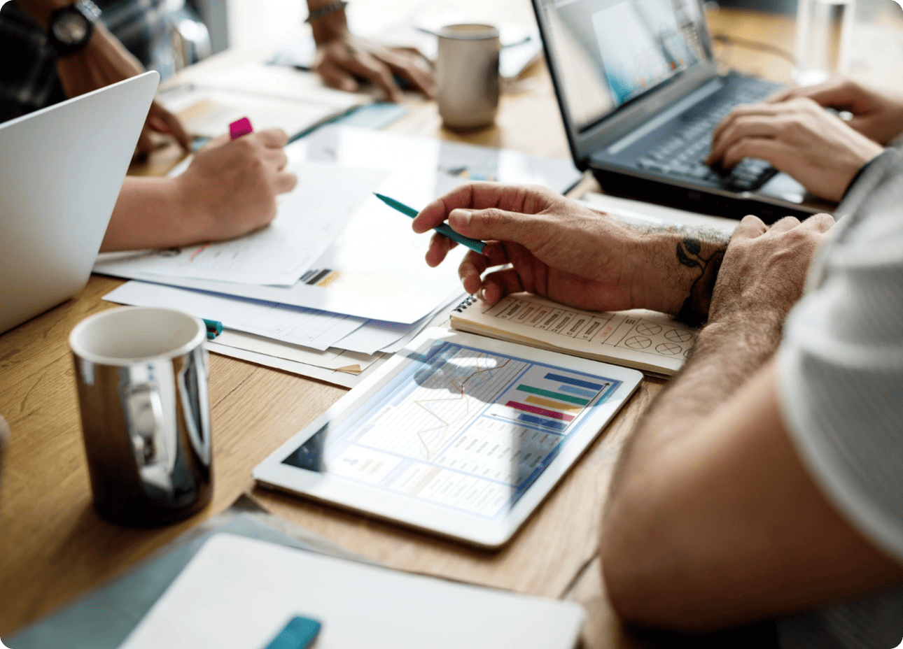 Gros plan sur une réunion de travail collaborative où une équipe analyse des graphiques de données sur une tablette et des ordinateurs.